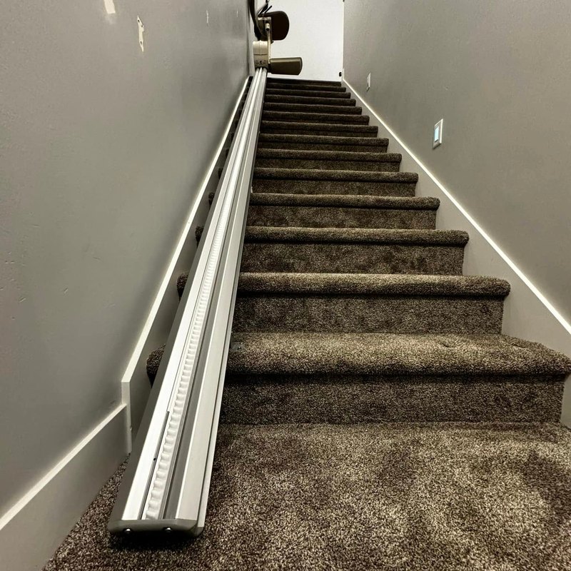 Stair lift rail running up a carpeted staircase between gray walls