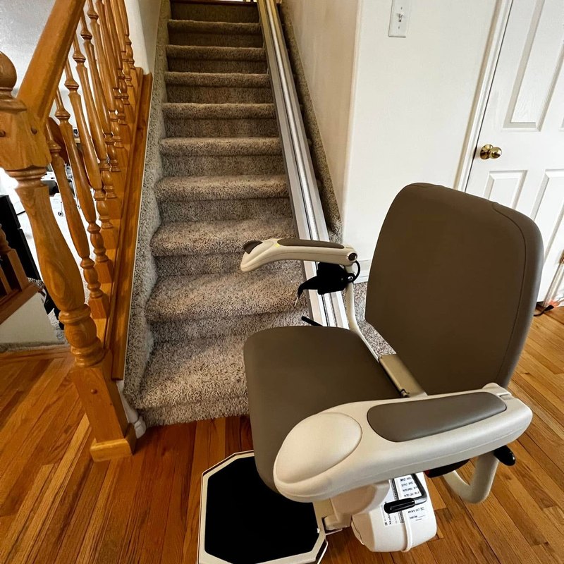Stair lift parked at the bottom of a carpeted staircase in a bright hallway