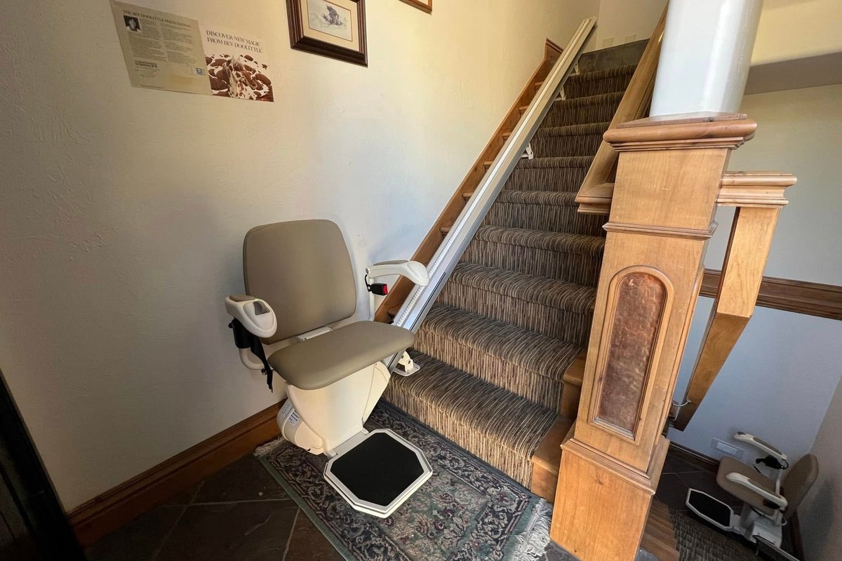 Harmar SL300 stair lift at the foot of a carpeted staircase beside a carved wood newel post