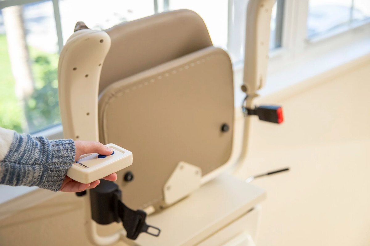 Hand pressing a Harmar remote control beside a folded stair lift seat