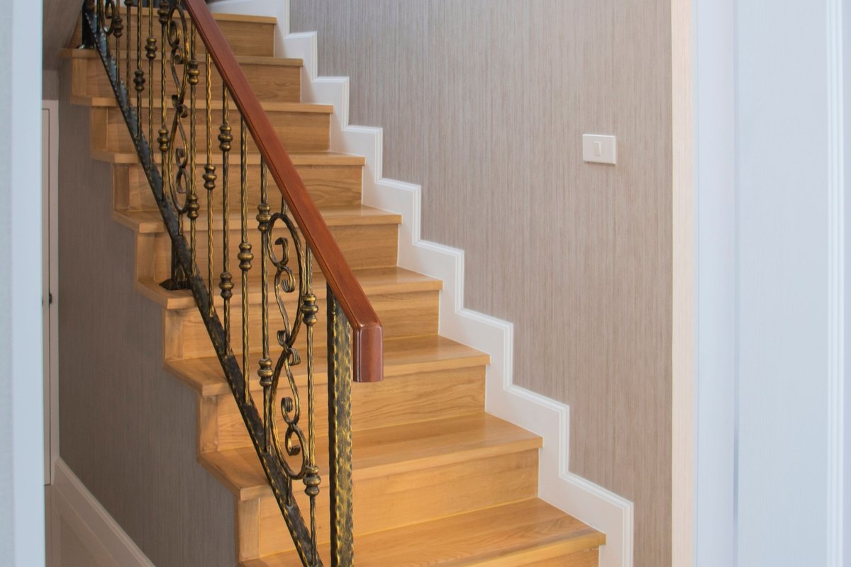 Sunlit straight wood staircase with an iron railing
